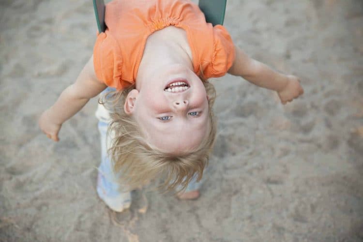 A child playing outdoors. A girl hanging upside down on a swing.