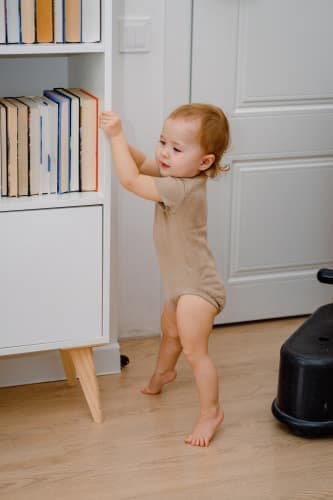 A cute baby learning to stand up or walking with support. First steps. Standing on toes abnormally.