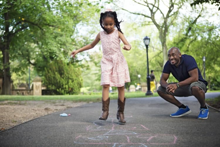 Father And Daughter Playing Hopscotch On Road At Park