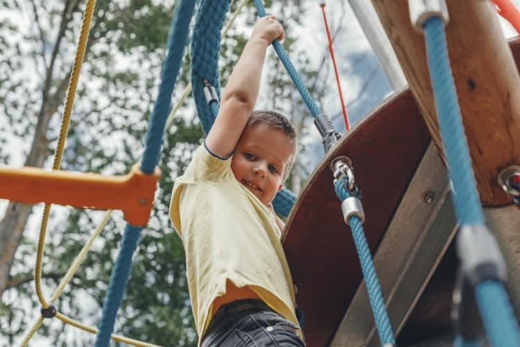 Cute Caucasian boy 6 years old playing on the playground in summer. Outdoor play, gross motor develo