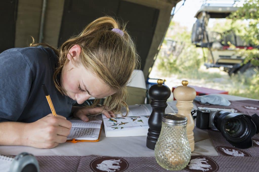A teenage girl writing in her journal in a tent.