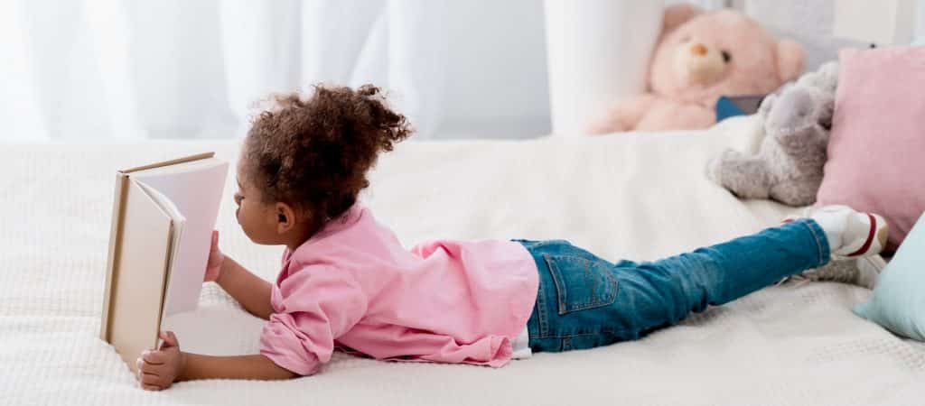 Adorable African american child lying on the bed and reading a book