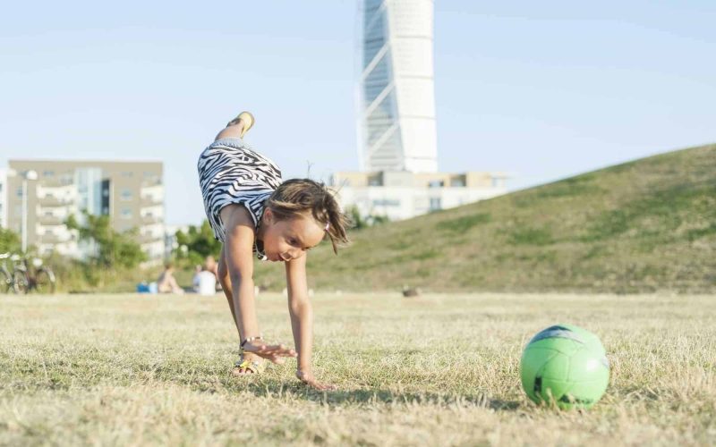 Little girl doing handstand on field in city