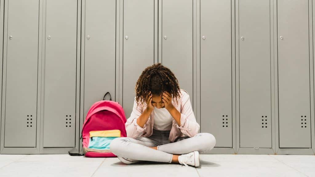 Troubles at school. Lonely sad african-american schoolgirl crying at school hall