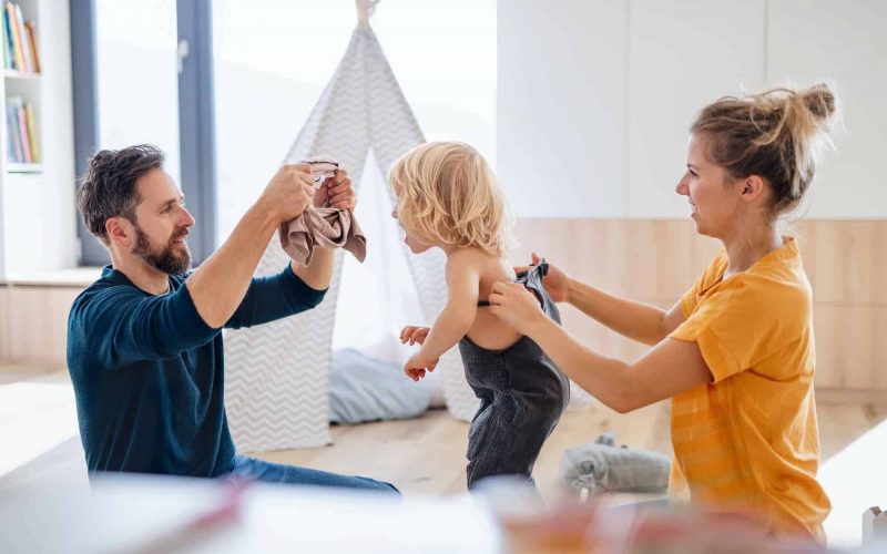 Young family with small child indoors in bedroom getting dressed.