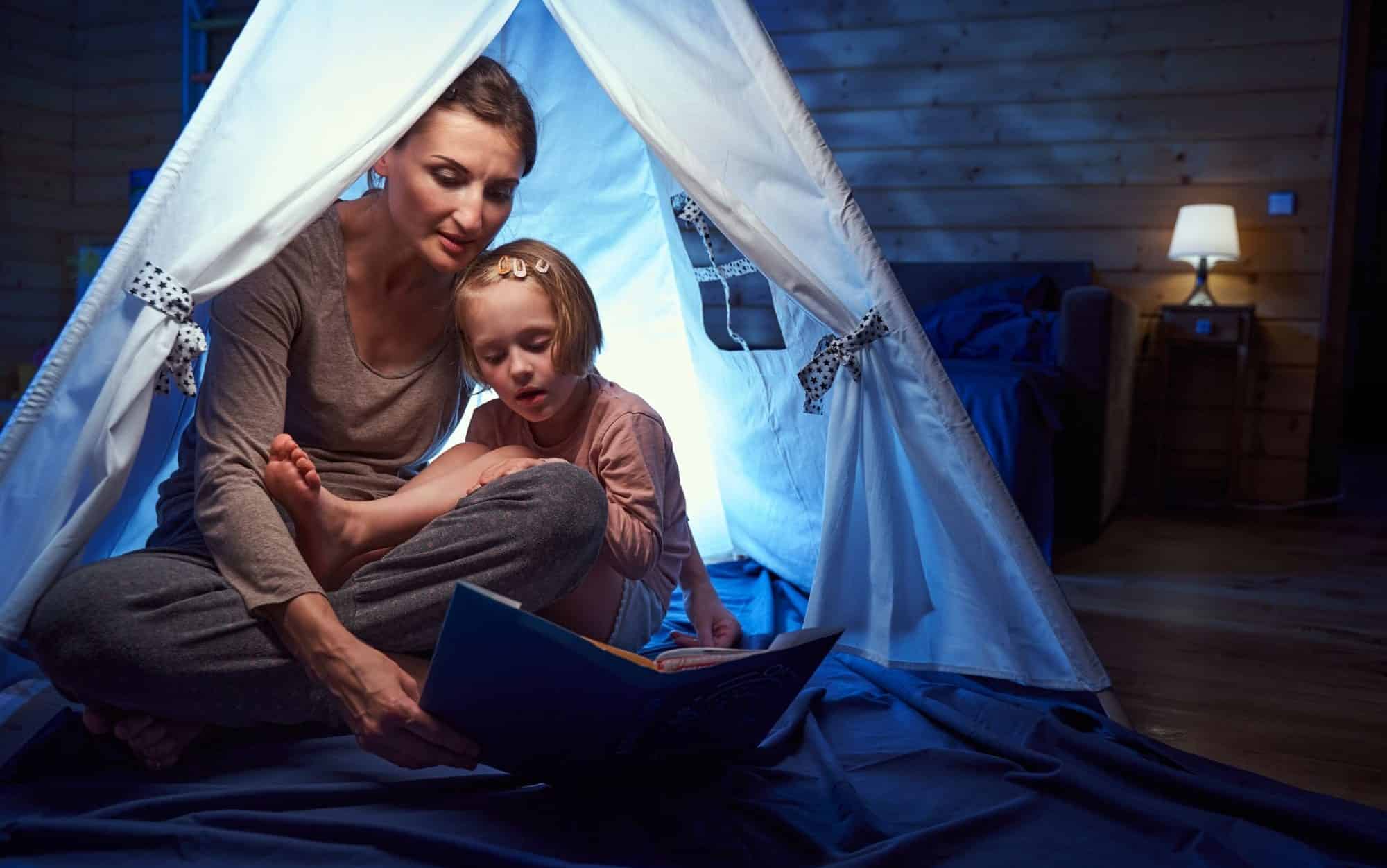 Adult and child in a tent at home reading book