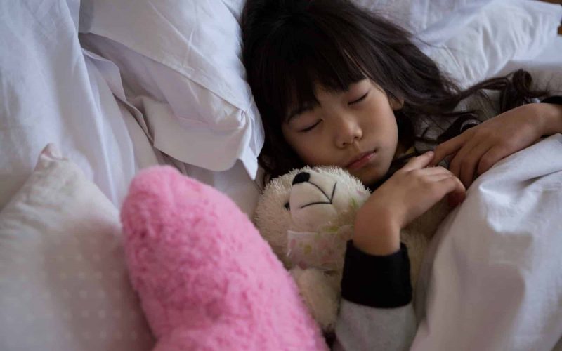 Girl with toys sleeping in bedroom