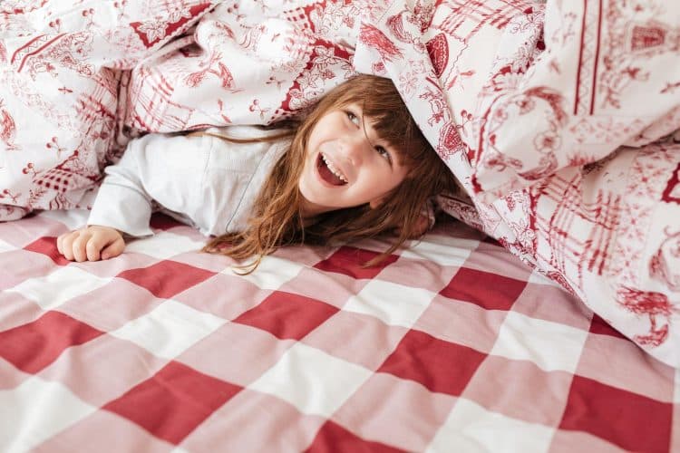 Happy child on bed under blanket