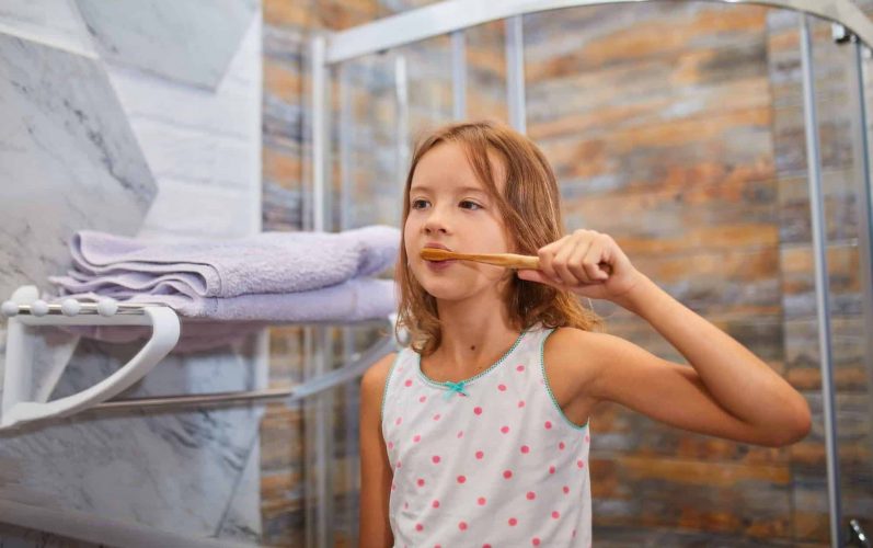 Little Girl brushing teeth with ecologe wooden Toothbrush in the bathroom