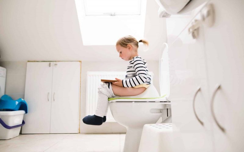 Little girl with tablet sitting on the toilet.