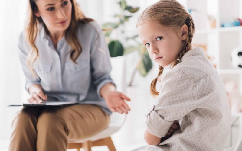 psychologist talking to angry child with crossed arms while she looking at camera