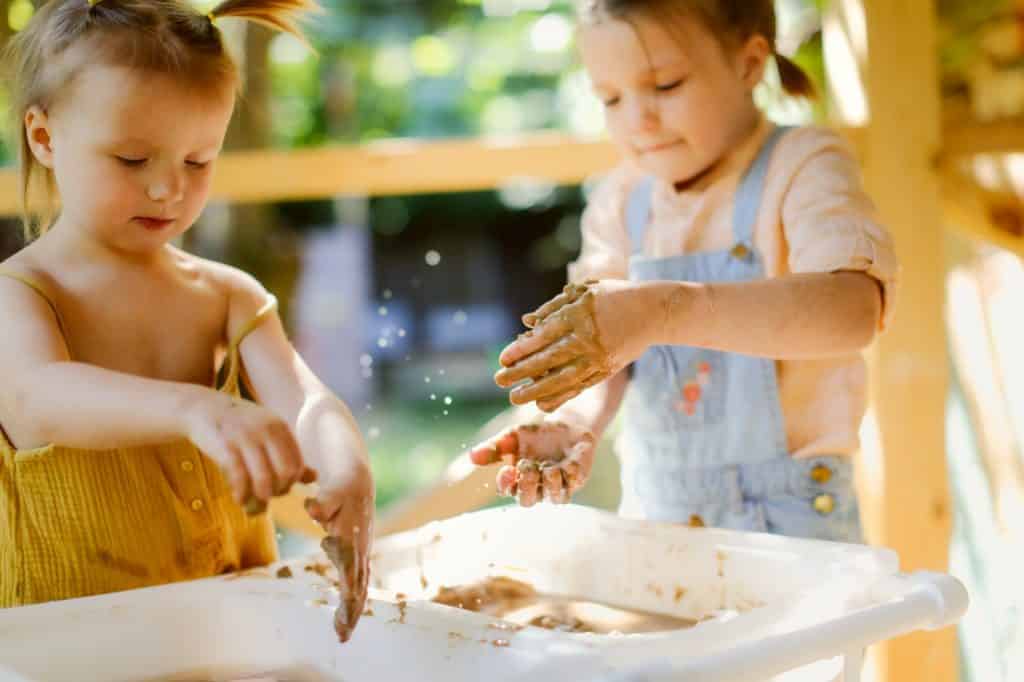 Happy children play with sand and water in sensory baskets on the outdoor sensory table,