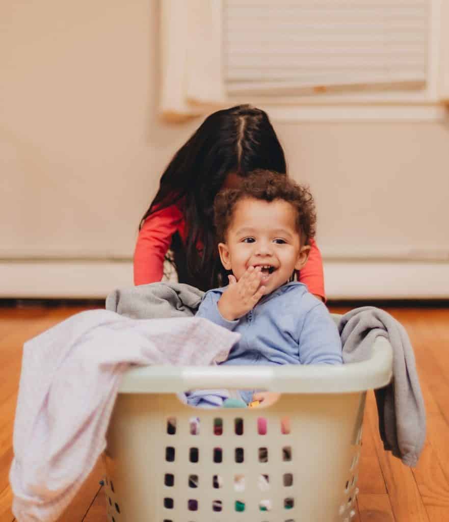 brother and sister at home having fun playing with laundry basket, sister pushing little brother