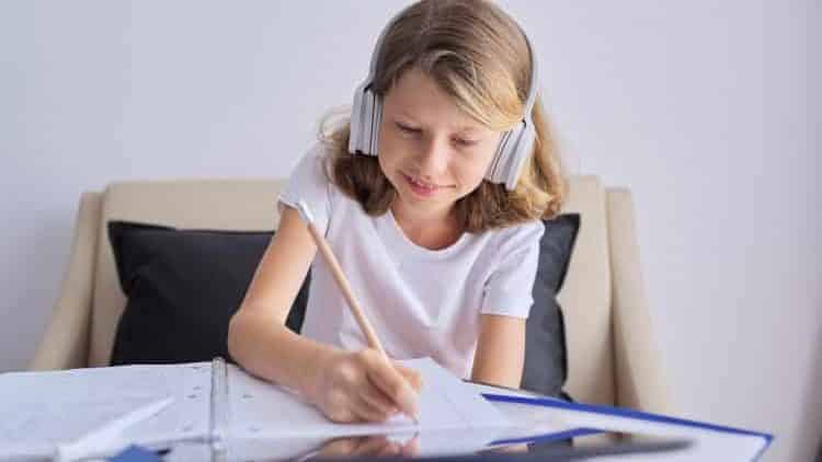 Child with digital tablet and headphones writing in notebook