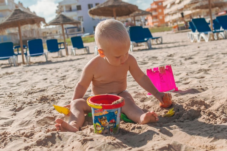 topless boy holding blue plastic bucket on sand during daytime