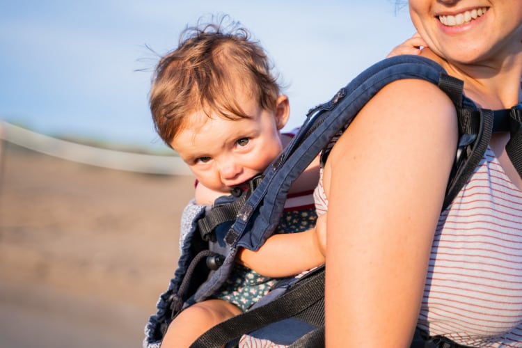 Baby chewing on the strap of a baby carrier outdoors