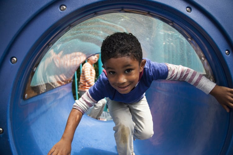 Boy bending forward emerging from playground tunnel