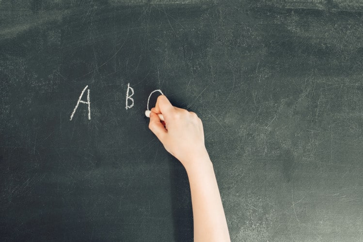 child's hand with chalk write alphabet on black chalkboard