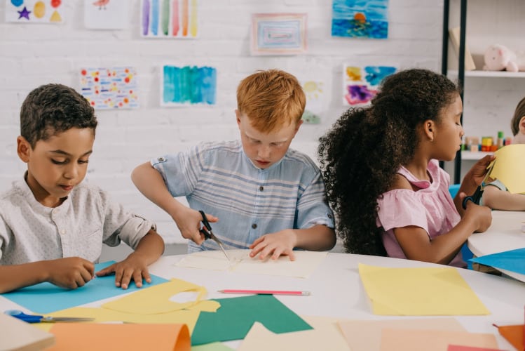 portrait of focused multiethnic kids with scissors making paper applique in classroom