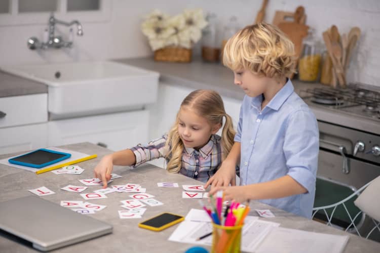 Two blond kids putting cards with letters on the table