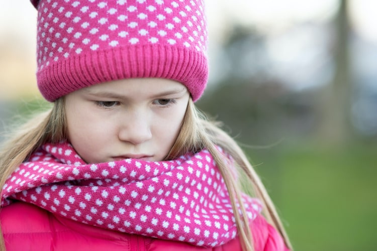 Sad child girl in warm knitted winter clothes outdoors.