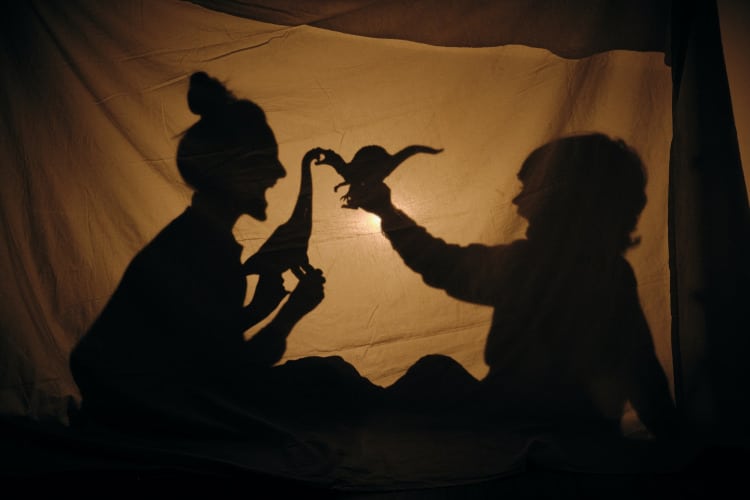 Silhouette of woman with kid playing behind sheet
