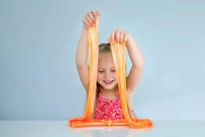 Cute funny girl play with orange slime. Kid squeeze and stretching toy slime.